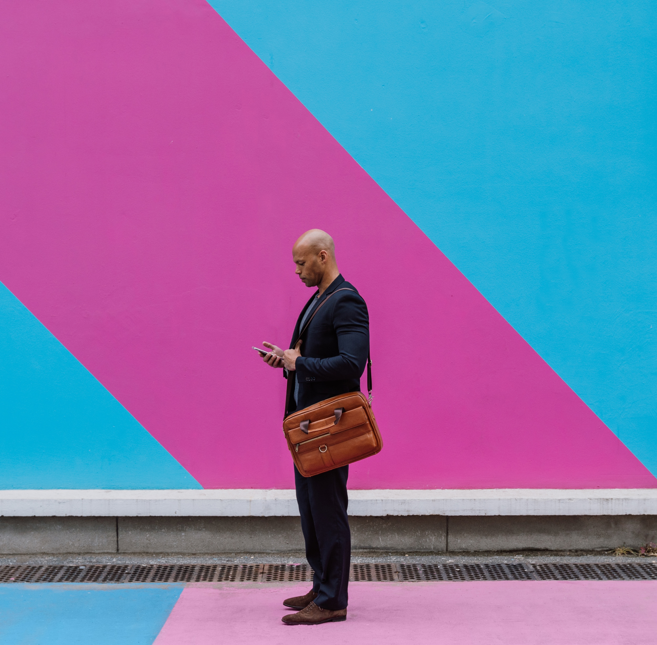 Man in a business suit with an over the shoulder bag standing on sidewalk looking at their phone